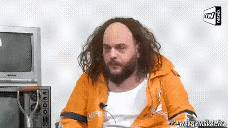 a man with long hair and a beard is sitting in front of a microwave and a tv