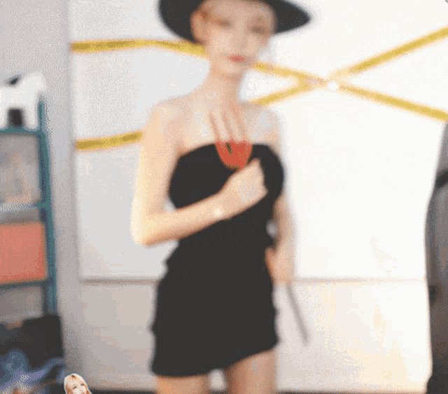 a woman in a black dress and hat is standing in front of a yellow tape