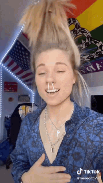 a woman wearing a blue shirt and a key necklace is holding a needle in her nose .
