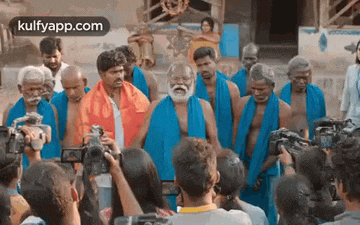a group of people are standing in front of a camera while a man with a beard is being interviewed .