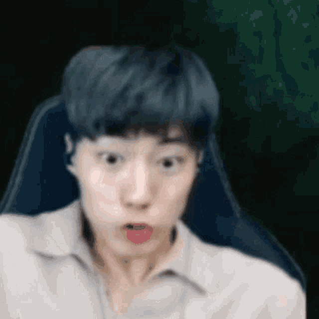 a young man with blue hair is sitting in a chair and making a funny face .
