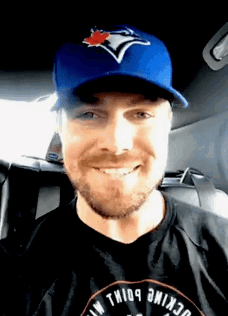 a man wearing a blue jays hat and a black shirt with the word genuine on it