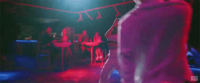 a man in a white shirt is dancing in a club with people sitting at tables behind him .