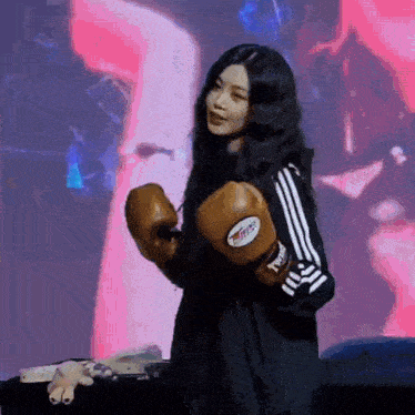 a woman wearing boxing gloves is standing in front of a stage .