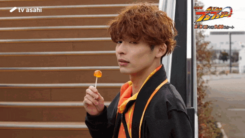 a man holding a lollipop in front of stairs with tv asahi in the corner