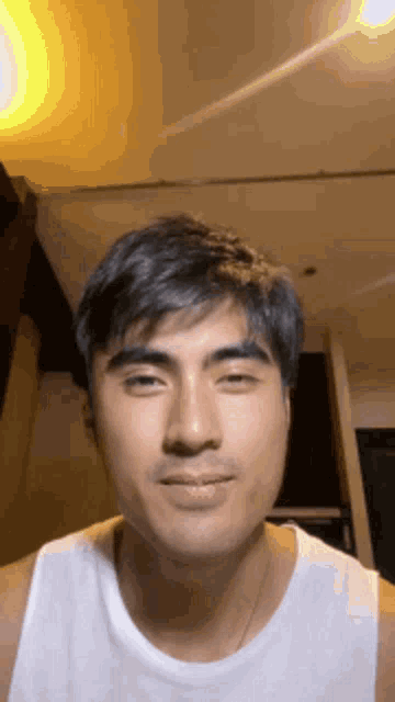 a man in a white tank top is looking at the camera .