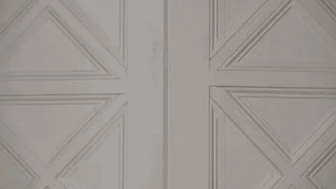 a man in a suit and beret is giving a thumbs up while peeking out of a doorway .