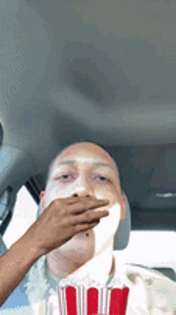 a man in a car is eating popcorn from a red and white striped bucket