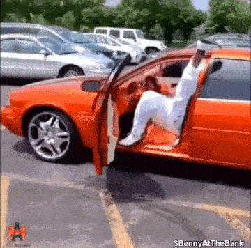 a man is getting out of a red car in a parking lot