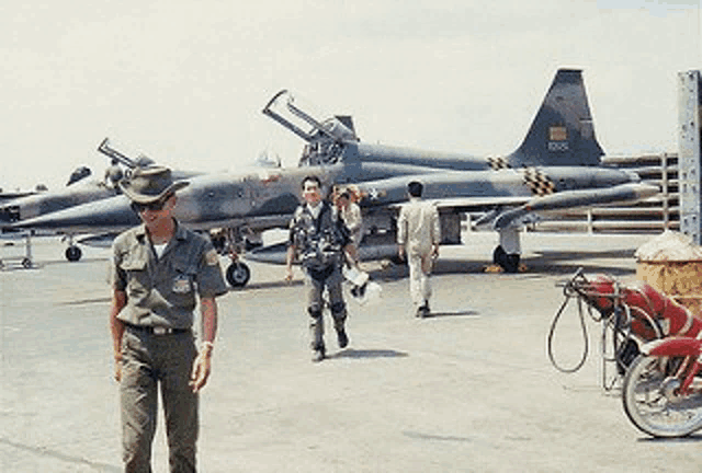 a man in a cowboy hat stands in front of a fighter jet with the numbers 3005 on the tail