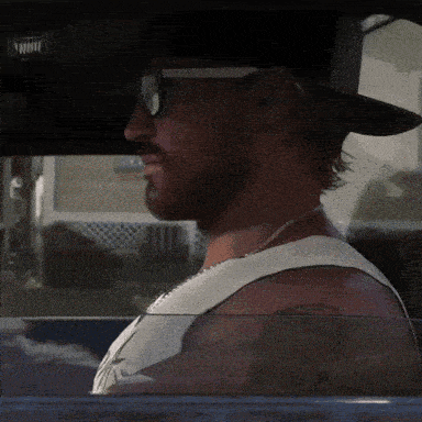 a man wearing sunglasses and a hat is looking out the window of a car