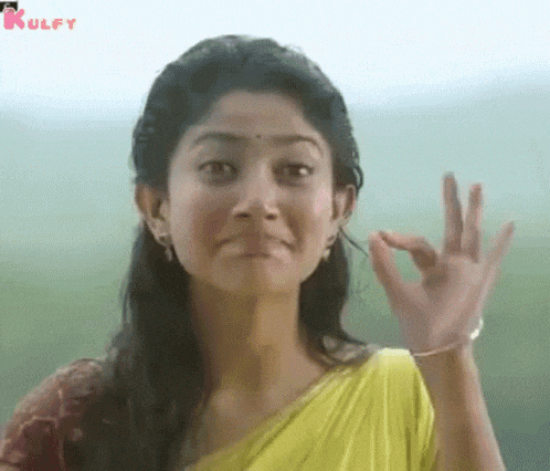 a woman in a yellow sari is making an ok sign with her hand .