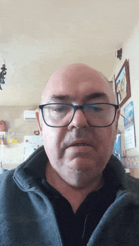 a bald man wearing glasses and a black shirt looks at the camera
