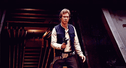 han solo from star wars is holding a gun in his hand while standing in a dark room .