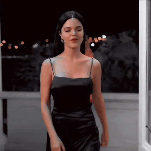 a woman in a black dress is standing in front of a window at night