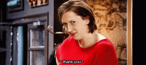 a woman in a red shirt is standing in front of a door and saying thank you .