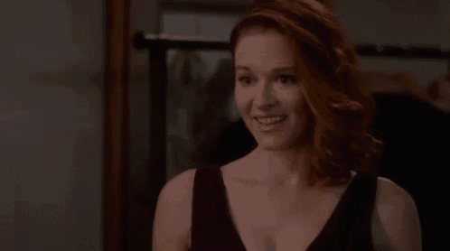 a woman with red hair is smiling and wearing a black tank top .