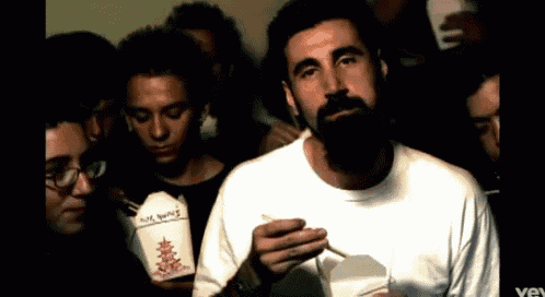 a man in a white shirt is eating chinese food from a box that says hot wings
