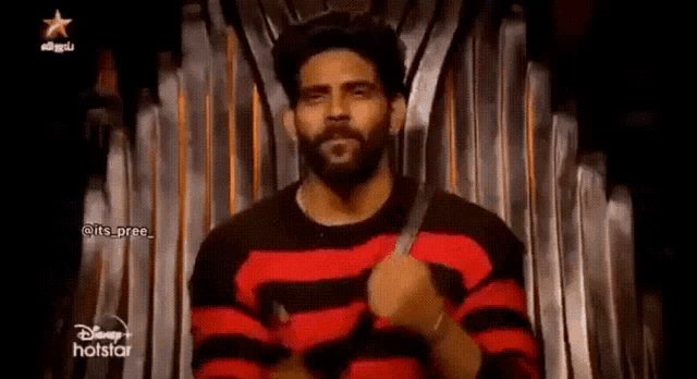 a man with a beard wearing a red and black striped sweater is holding a knife .