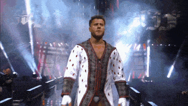 a man in a plaid coat is walking on a stage in front of the word reigns