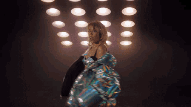 a woman wearing a holographic jacket is dancing in front of a row of lights
