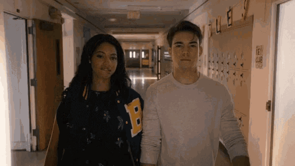 a boy and a girl are walking down a hallway .