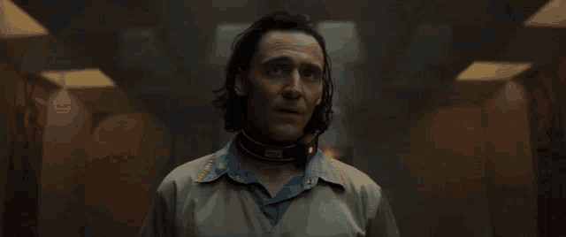 a man with long hair and a collar around his neck is smiling in a dark room .