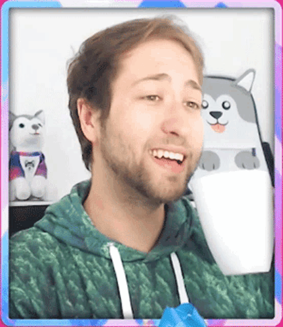 a man in a green hoodie is smiling in front of a stuffed dog