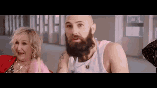 a bald man with a beard is sitting next to a woman in a room .
