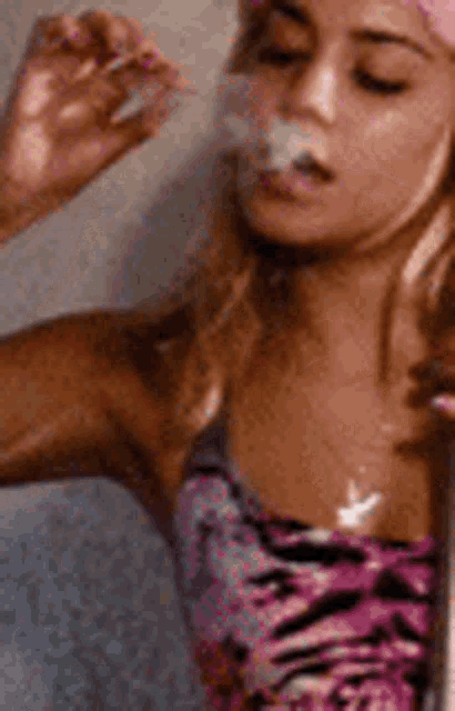 a woman is smoking a cigarette in a pink hat .