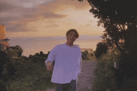 a man in a white shirt is walking down a path in front of a sunset