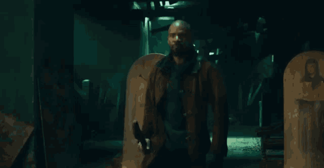 a man with a beard is standing in a dark room holding a large axe .