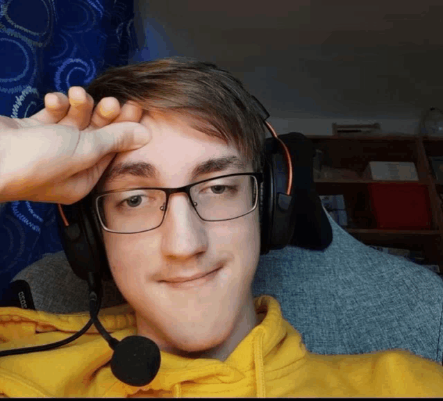 a young man wearing glasses and headphones holds his hand to his head