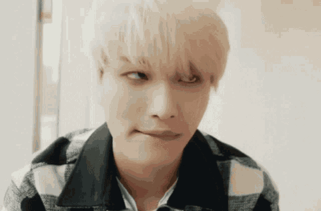 a young man with blonde hair is making a funny face and wearing a plaid shirt .