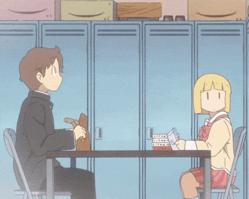 a boy and a girl are sitting at a table in front of lockers with boxes on top of them