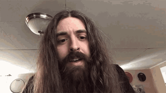 a man with long hair and a beard is standing in front of a drum set