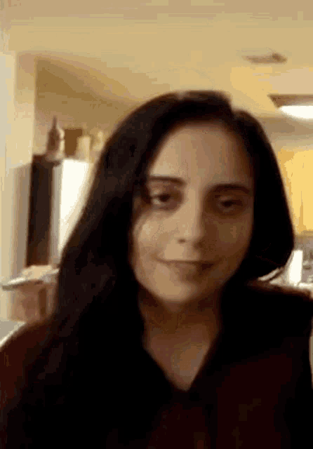 a woman with long black hair is making a funny face while standing in a kitchen .