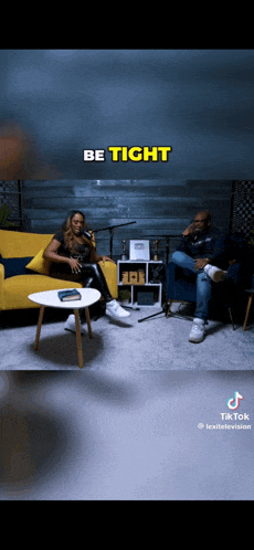 a man and a woman are sitting on a couch in front of a microphone in a living room .