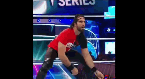 a wrestler in a red shirt is kneeling down in a ring .