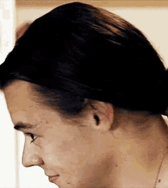 a close up of a man 's face with his hair in a bun and a necklace .