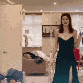 a woman in a black dress is standing in a living room holding a cell phone .