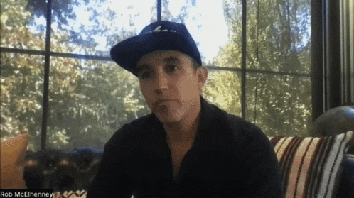 a man wearing a hat is on a video call with the name rob mcelhenney at the bottom
