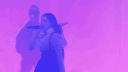 a woman sings into a microphone while a man plays a guitar in the background