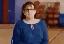 a woman wearing glasses and a blue shirt is standing in front of a wall .