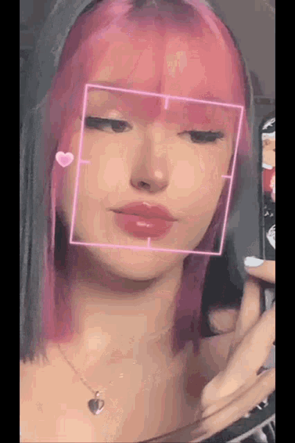 a girl with pink hair and a heart necklace is taking a selfie with her phone .