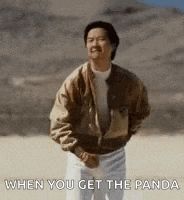 a man in a jacket and white pants is dancing in a desert .