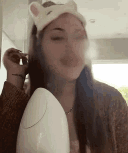 a woman wearing a headband with cat ears is using a steamer to clean her face .