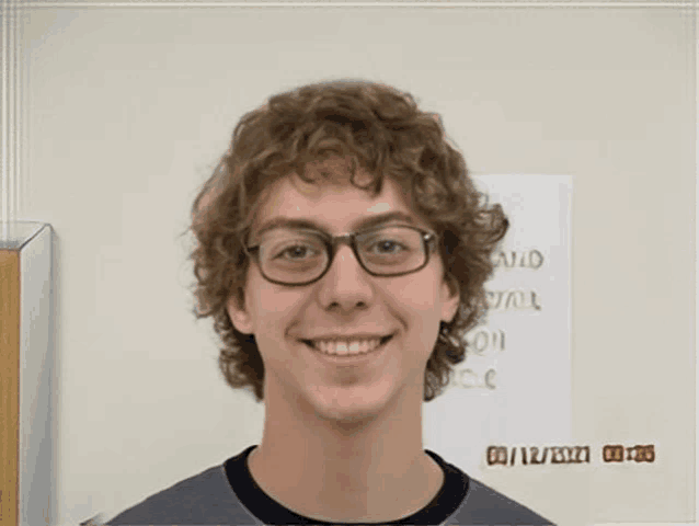 a young man with curly hair and glasses smiles in front of a sign that says " said " on it
