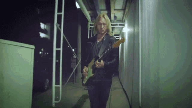 a man in a black leather jacket is playing a guitar in a dark hallway