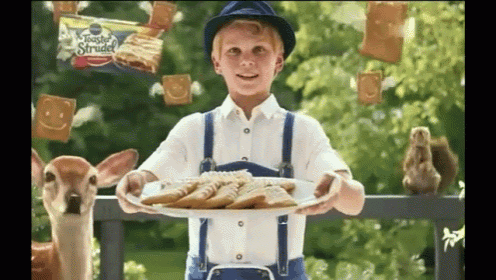 a boy holding a plate of cookies with a bag of toaster strudel behind him